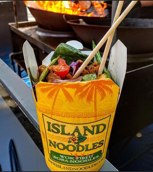 cup of island noodles in front of the fiery wok